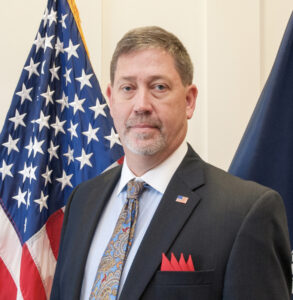 An image of Mr. Dennis L. Bacon posed in front of a US flag