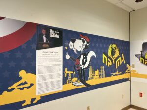 An image of a decorated wall with graphics from NPMC and our founder Jack Lavin, the NPMC logo, and a cartoon POL cat