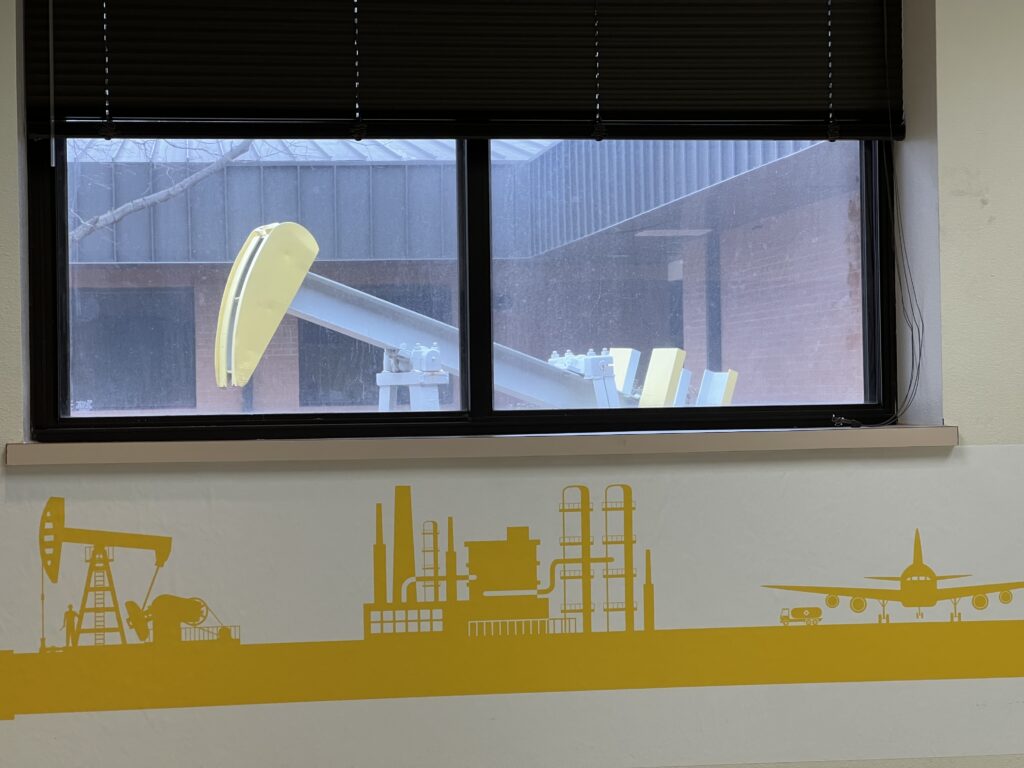 An image of a decorated wall with a graphic of an oil derrick in yellow that mirrors the model oil derrick that is seen through the window above the graphic